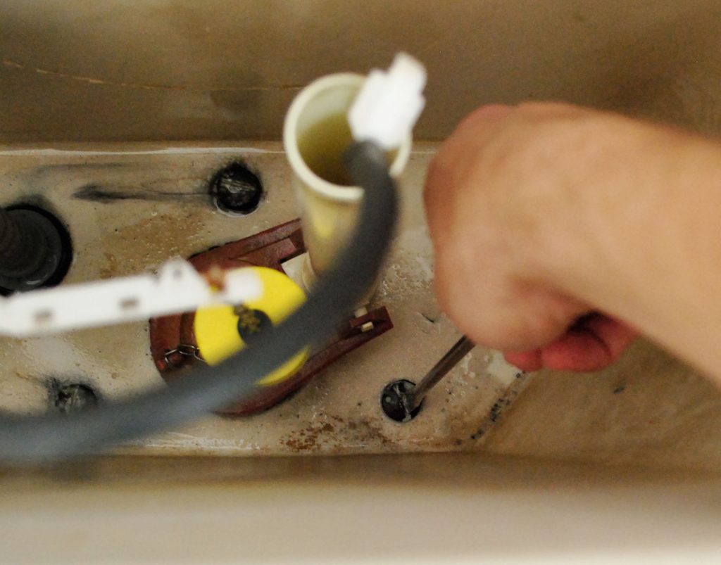 Hand With Screwdriver Adjusting Bolts In Toilet Tank