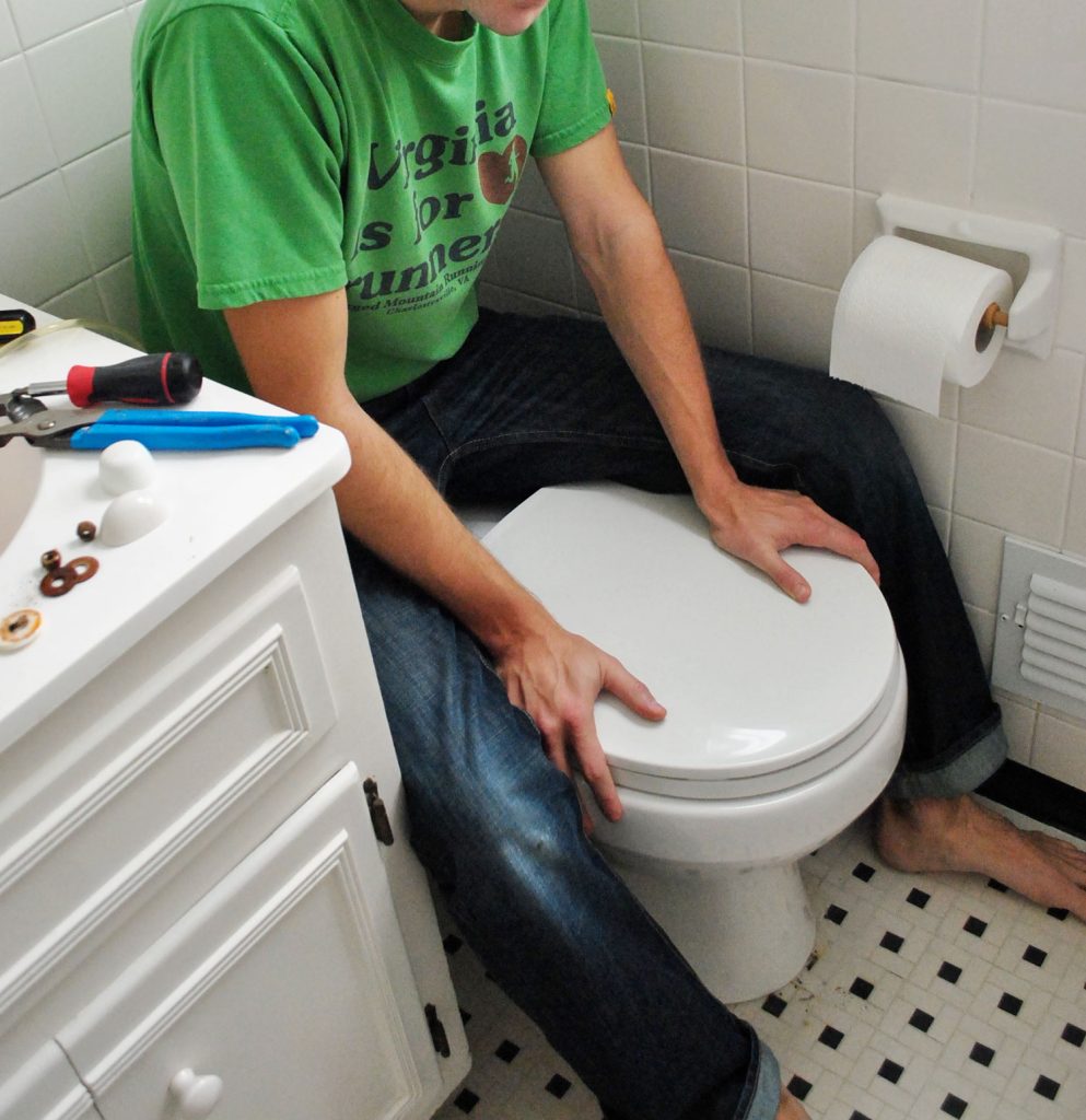 John Sitting On Back of Toilet Bowl To Press Into Place