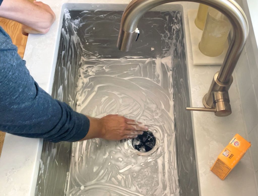 Hand scrubbing a stainless steel sink clean with baking soda