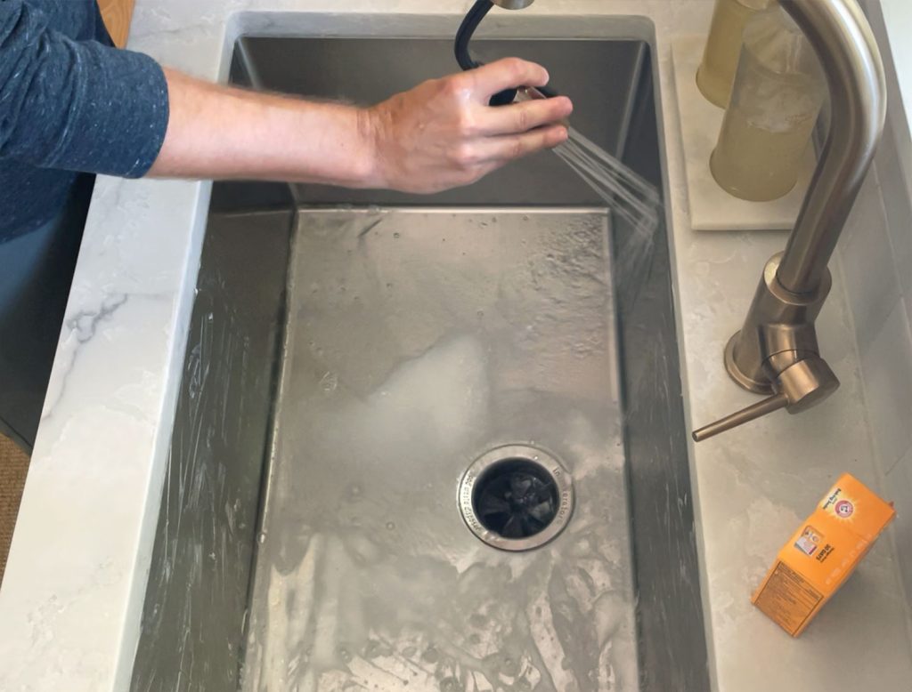 Rinsing stainless steel sink with warm water from faucet