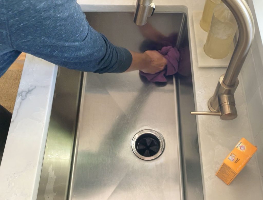 Buffing cleaned stainless steel sink dry with rag