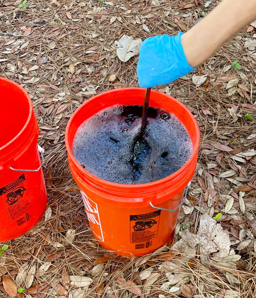 Hand Stirring Bucket Of Black Rit Fabric Dye With Clothes Inside